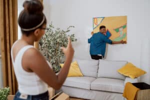 man hanging up art in his house with his wife watching